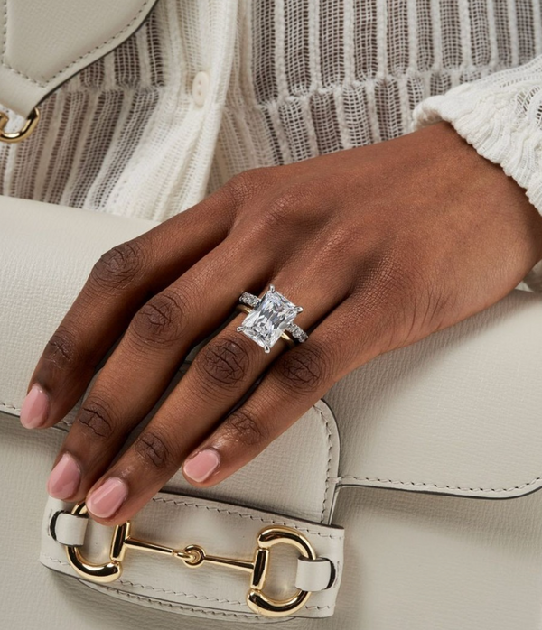 hand holding a handbag and wearing lily arkwright 5ct large moissanite radiant cut engagement ring with thin platinum or white gold band stacked with moissanite eternity band