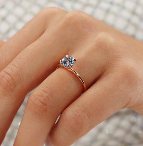 hand wearing dainty aquamarine or aqua spinel 18k rose gold four prong engagement ring 