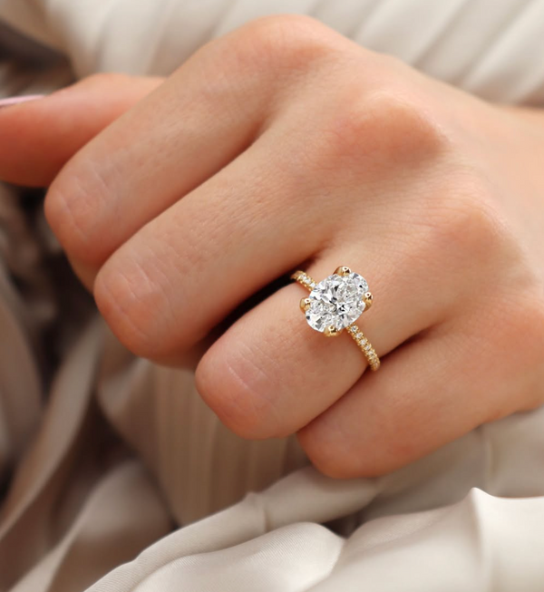 hand wearing oval lab diamond engagement ring with thin 18k yellow gold diamond pave band 