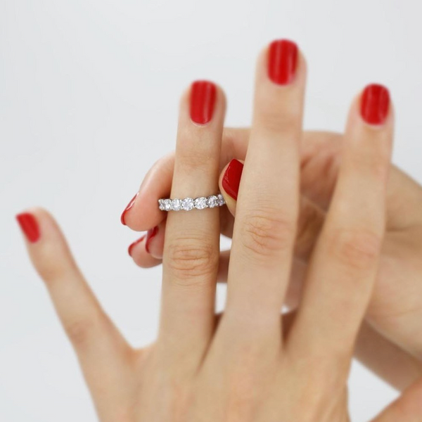 two hands putting on large diamond set eternity band with shared prong setting