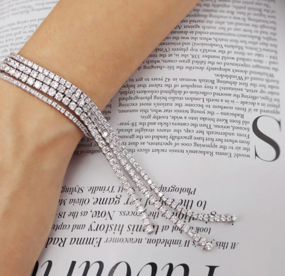 arm wearing multiple tennis bracelets draped over magazine