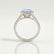 Amelia halo engagement ring with a round aquamarine-blue lab-grown sapphire centre stone and diamond accents, side profile showing the setting and band.