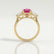 Blossom trilogy engagement ring in 18k yellow gold with a round pink lab-grown sapphire centre stone and pear-shaped diamond side stones, side profile showing the setting and band.