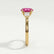 Blossom trilogy engagement ring in 18k yellow gold with a round pink lab-grown sapphire centre stone and pear-shaped diamond side stones, end-on view showing the setting and band.