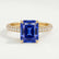 Coco hidden halo engagement ring in 18k yellow gold with a radiant blue lab-grown sapphire centre stone and diamond accents on a triple pavé band, front view.