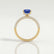 Coco hidden halo engagement ring in 18k yellow gold with a radiant blue lab-grown sapphire centre stone and diamond accents on a triple pavé band, side profile showing the setting and band.