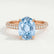Coco hidden halo engagement ring in 18k rose gold with an oval aquamarine-blue lab-grown sapphire centre stone and diamond accents on a triple pavé band, front view.