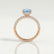 Coco hidden halo engagement ring in 18k rose gold with an oval aquamarine-blue lab-grown sapphire centre stone and diamond accents on a triple pavé band, side profile showing the setting and band.