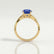 Eden vine solitaire engagement ring in 18k yellow gold with an oval blue lab-grown sapphire centre stone and diamond accents, side profile showing the setting and band.