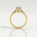 Isabella solitaire engagement ring in 18k yellow gold with an oval aquamarine-blue lab-grown sapphire centre stone, end-on view showing the setting and band.