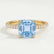 Lively hidden halo engagement ring in 18k yellow gold with a cushion aquamarine-blue lab-grown sapphire centre stone on a pavé-set band, front view.