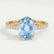 Lively hidden halo engagement ring in 18k yellow gold with an oval aquamarine-blue lab-grown sapphire centre stone on a pavé-set band, front view.