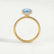 Lively hidden halo engagement ring in 18k yellow gold with an oval aquamarine-blue lab-grown sapphire centre stone on a pavé-set band, side profile showing the setting and band.