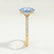 Lively hidden halo engagement ring in 18k yellow gold with an oval aquamarine-blue lab-grown sapphire centre stone on a pavé-set band, end-on view showing the setting and band.