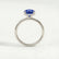 Paris hidden halo engagement ring in 18k white gold with an oval blue lab-grown sapphire centre stone and diamond accents, side profile showing the setting and band.