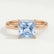 Paris hidden halo engagement ring in 18k rose gold with a princess-cut aquamarine-blue lab-grown sapphire centre stone and diamond accents, front view.