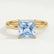 Paris hidden halo engagement ring in 18k yellow gold with a princess-cut aquamarine-blue lab-grown sapphire centre stone and diamond accents, front view.