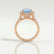 Rosa halo engagement ring in 18k rose gold with an oval aquamarine-blue lab-grown sapphire centre stone and diamond accents, side profile showing the setting and band.