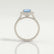Violette halo engagement ring with a cushion aquamarine-blue lab-grown sapphire centre stone and diamond accents, side profile showing the setting and band.